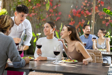 Young waiter talking to restaurant guests - taking orders for food and drinks