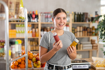 Youth girl spouses hold bottles and choose consider smoothie in store. Market visitor pick up...