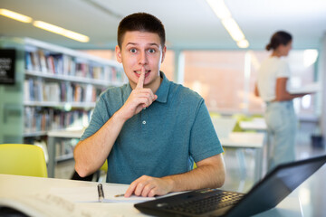Obraz premium Young man calls for silence in the public library - puts his index finger to his lips