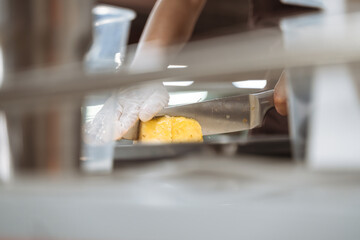 Closeup of a person wearing gloves slicing a piece of pineapple with a large knife in a kitchen setting.