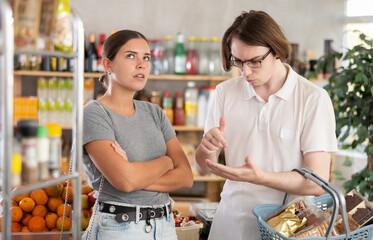 Irritated young man and young woman shoppers quarreling in grocery store