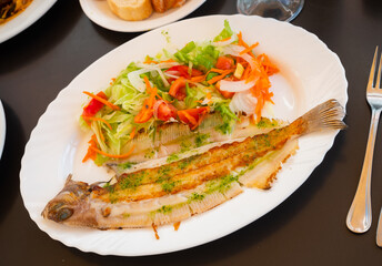 Carcass of fried fish is complemented by portion of their fresh vegetable salad. Fried fish carcass, composition of grated carrots, Chinese cabbage leaves, tomatoes, black olives.