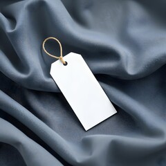 Blank white tag with gold string, smooth gray satin fabric background, soft folds and wrinkles, minimalist product photography, high contrast, studio lighting, close-up detail