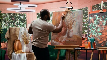 In an art studio, artist mixes a variety of watercolor paints on a palette to create a rustic...