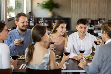 Group of men and women friends eating drinking and talking in restaurant