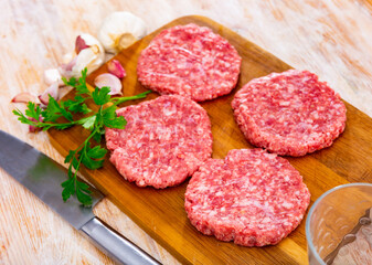 Uncooked healthy burgers on a chopping board served with heads of garlic, peppercorns, on a wooden tabletop at the restaurant