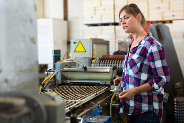 Confident woman machine operator working with automatic conveyor filling and seeding of plants in...