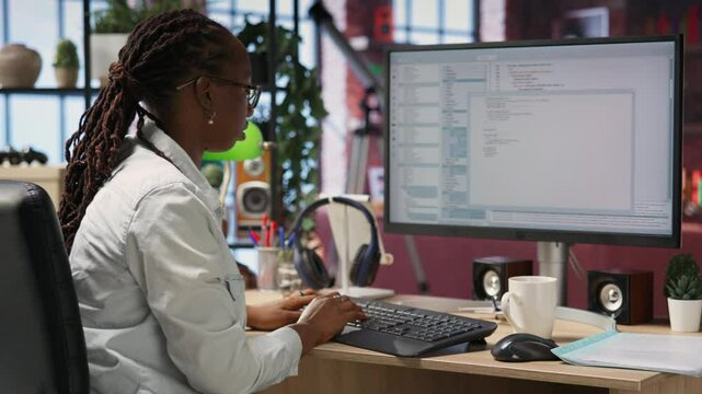 Engineer in home office looks at UI on computer monitor, typing and executing programming code. Panning shot of IT worker using coding application to write and test code in modern apartment, camera B