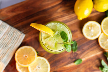 A refreshing green lemonade served in a glass with ice, garnished with mint and lemon slices,...