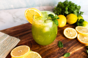 A refreshing green lemonade served in a glass with ice, garnished with mint and lemon slices,...