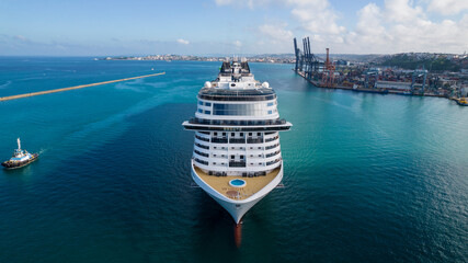 Bow, front view of large luxurious cruise ship sailing in the port of Salvador for anchorage, passenger ship arriving at harbor with container port cranes in the background