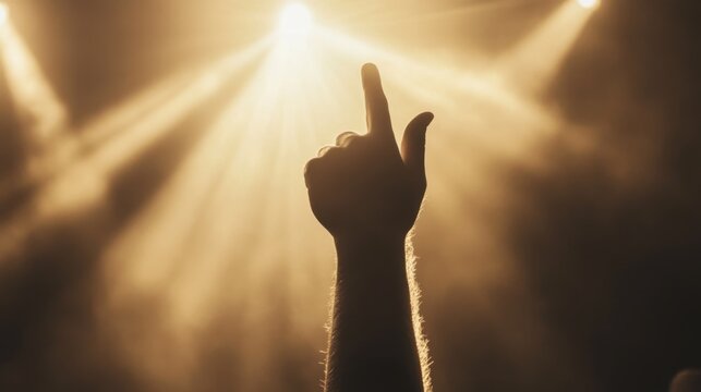 Silhouetted hand raised with index finger pointing up, illuminated by stage lights.