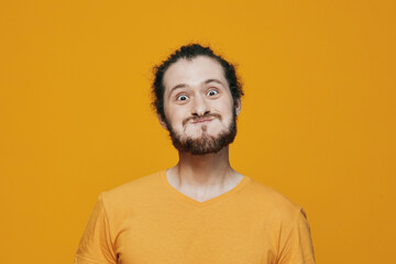 Fototapeta premium Young man with an expressive face making a funny grimace in a vibrant orange t shirt against a bold yellow background, showcasing joy and playfulness