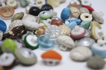 Close-up photography of assorted colorful buttons arranged on a white surface. A mix of textures, shapes, and materials create an interesting and vibrant composition for crafting or sewing concepts.
