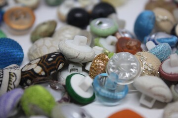 Close-up photography of assorted colorful buttons arranged on a white surface. A mix of textures, shapes, and materials create an interesting and vibrant composition for crafting or sewing concepts.