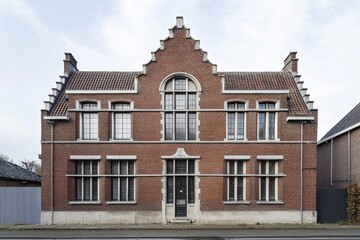 Fototapeta premium A charming red brick house, showcasing classic gable roof architecture, nestled in a serene neighborhood under a blanket of gray clouds