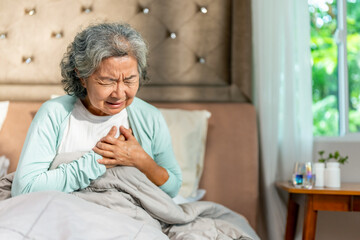 Diseases illness, heart attack and emergency medical healthcare in elderly. Asian senior woman suffering, feeling pain on chest area and difficulty breathing on the bed. Health insurance concept.