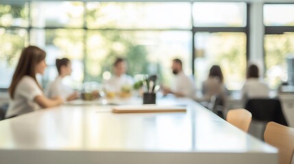 Blurred image of a group of people in a meeting around a large white table in a bright office.