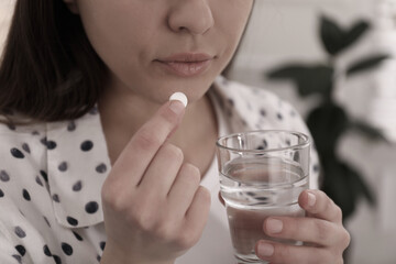Young woman taking pill indoors, closeup. Toned for dramatic atmosphere