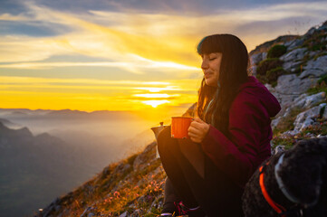 Obraz premium Young woman enjoying a hot beverage during a mountain camping trip at sunset