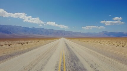 Naklejka premium Empty desert highway stretching into the horizon with mountains in the distance.