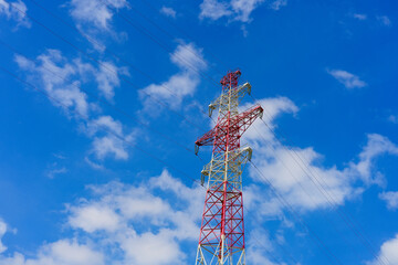 A tall electrical transmission tower is prominently featured against a vibrant blue sky filled with...