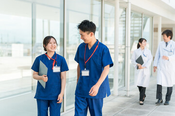 病院の通路で話す医者・医師・看護師・医療従事者・ドクター・作業療法士・理学療法士の男女

