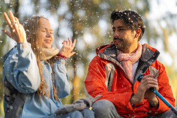 Cheerful couple sitting outdoors during snowfall, smiling and enjoying the winter weather. A heartwarming scene of togetherness and adventure in a cold yet serene environment.
