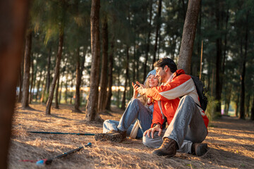 Couple sitting on the forest floor, enjoying a peaceful moment in the golden light of the setting sun. A serene outdoor scene of friendship, exploration, and nature's beauty.