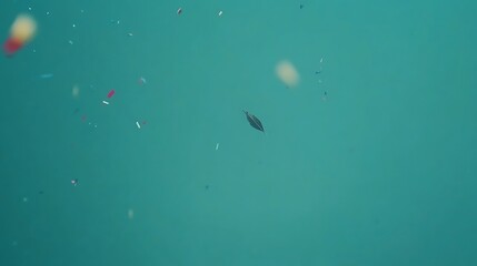 Fototapeta premium A Single Feather Falls Through Teal Water With Confetti