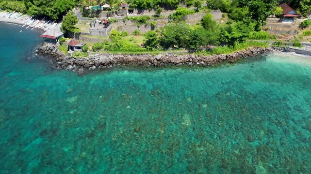 4K drone video of Ibus Beach, with a view of the turquoise blue ocean water surrounded by dramatic green mountain landscapes in Amed, East Bali Indonesia