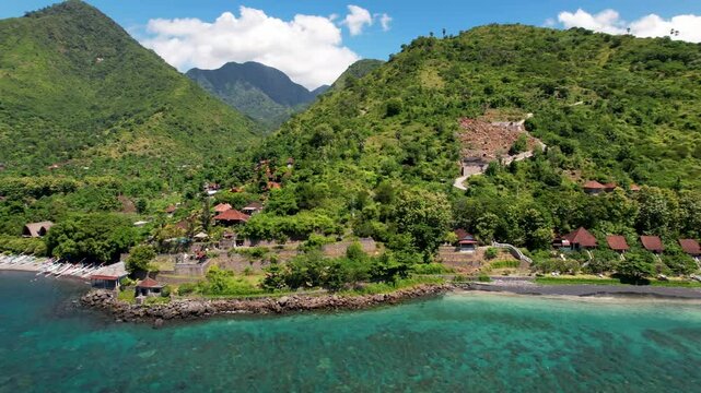 4K drone video of Ibus Beach, a black sand beach with turquoise blue ocean water surrounded by dramatic green mountain landscapes in Amed, East Bali Indonesia