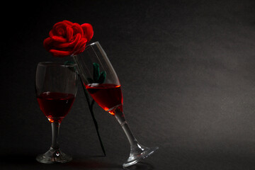 Negative Space two wine glasses toasting each other and one rose standing on both sides of the wine glass on black background, dark black background