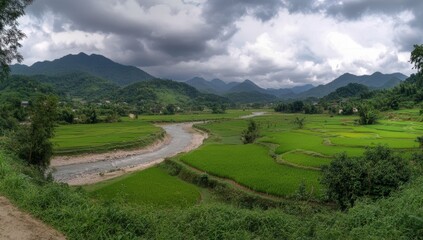 Obraz premium Panoramic view of a serene river winding through lush green rice paddies and verdant mountains under a dramatic sky.