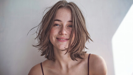 A young woman with shoulder-length, tousled brown hair. She has a gentle smile on her face and is looking directly at the camera
