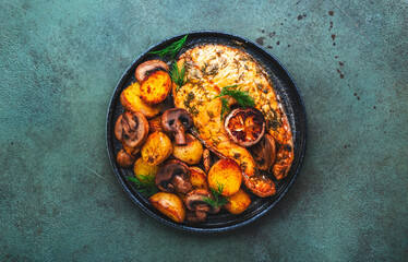 Baked salmon with lemon and dill, fried potatoes with mushrooms and cream sauce. Green rustic background, top view