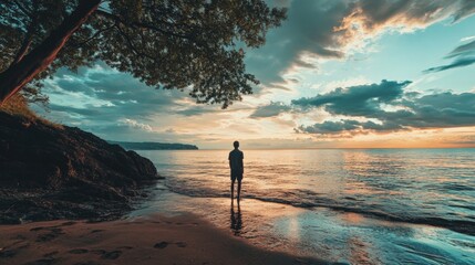 Silhouette of a person standing on a beach during sunset, looking out at the lake