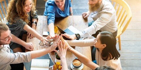 Group of diverse people high five around table with coffee and notebooks, showing teamwork and collaboration casual meeting setting. Group of diverse friends hands together over the table as teamwork