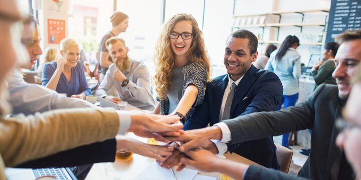 Diverse group in a casual meeting, hands in center, teamwork and collaboration. Smiling teamwork in a cafe. Collaboration and unity in business. Diverse men and women hands together for teamwork