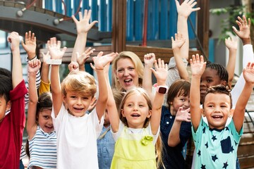 Group of diverse children, boys and girls, with Caucasian woman teacher, smiling and raising hands....