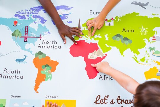 Children's hands exploring a colorful world map. Kids pointing at continents like Africa, Europe, and Asia. Educational map for children learning geography. Geography class in school with map.