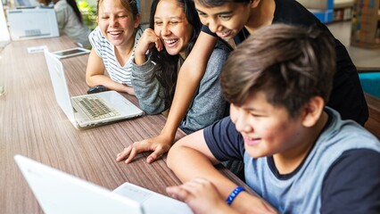 Group of diverse kids using laptops, smiling and watching together. Engaged children, technology, and education. Happy students collaborating on computers. Diverse kids watching video on laptop.