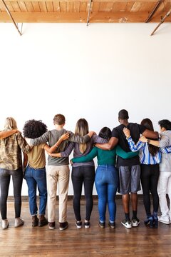 A diverse group of people standing together, arms linked, facing away. Unity and diversity in this group photo, emphasizing togetherness and support. Diverse people standing together as community.