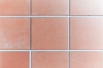 A close-up view of a textured tiled surface, featuring square tiles in warm hues arranged in a grid pattern.