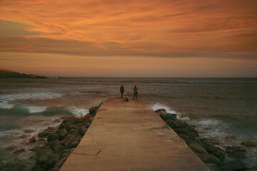 silhouette of two unrecognizable women fishing on a pier at sunset