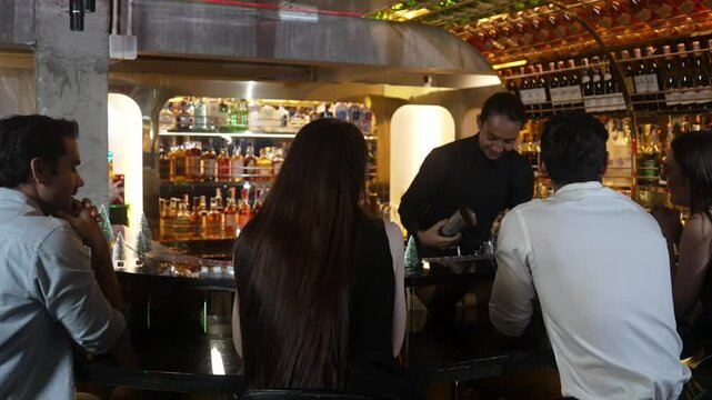 Smiling Asian bartender taking shaker preparing mixed cocktail at decorated christmas tree counter bar while talking to VIP guest. Special refresh drink showcasing nightlife at pub luxury. Vinosity.