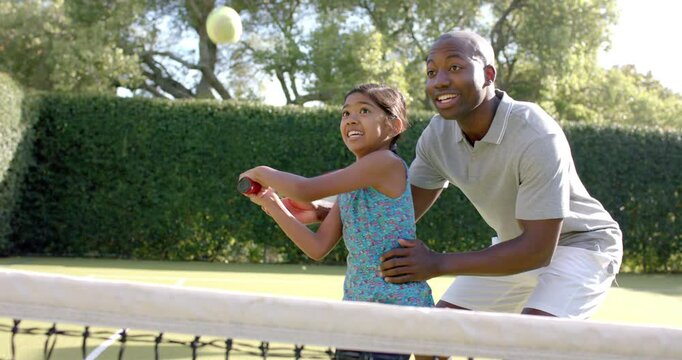 Playing tennis, father teaching daughter how to hit ball on court
