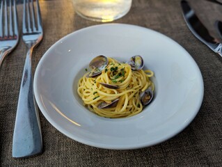 Spaghetti alle vongole seafood pasta with clams and parsley served on white plate with fork and knife