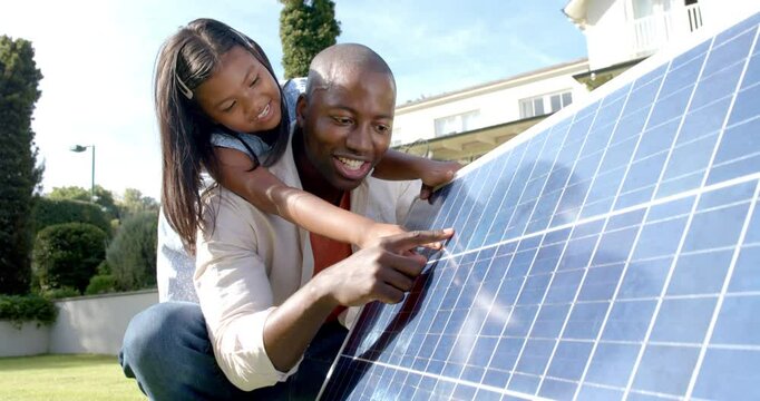 Father and daughter examining solar panel together, learning about renewable energy