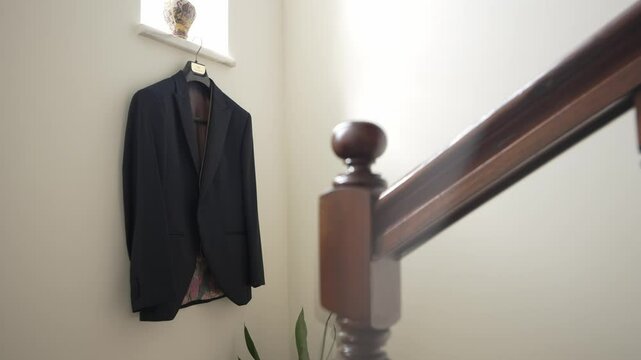 black suit jacket on a hanger near a wooden staircase in a bright, minimalist hallway